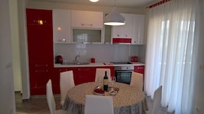 A modern kitchen with white and red cabinetry, a dining table with chairs, and a kitchen island with a wine bottle and glasses.