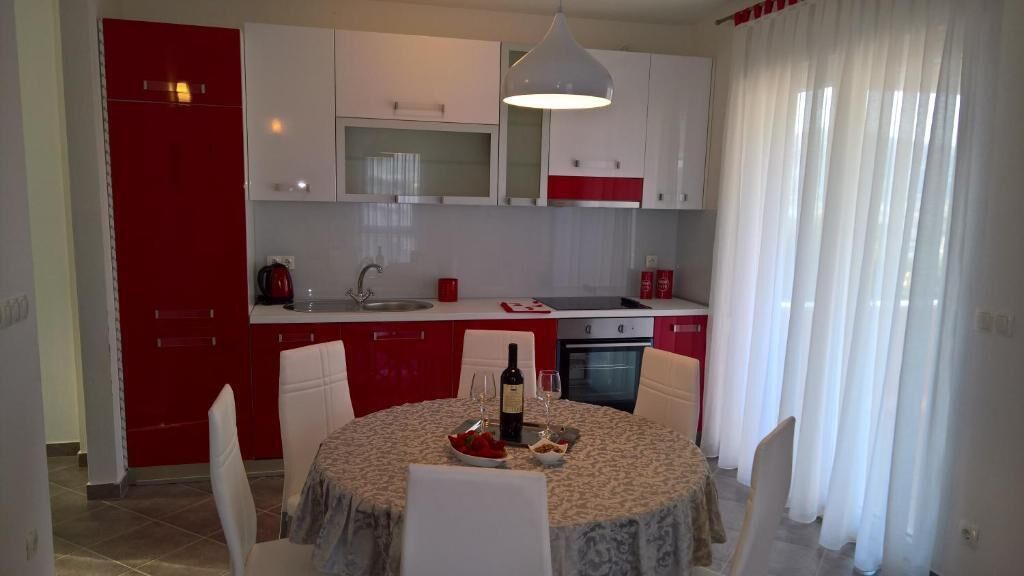 A modern kitchen with white and red cabinetry, a dining table with chairs, and a large window with sheer curtains.