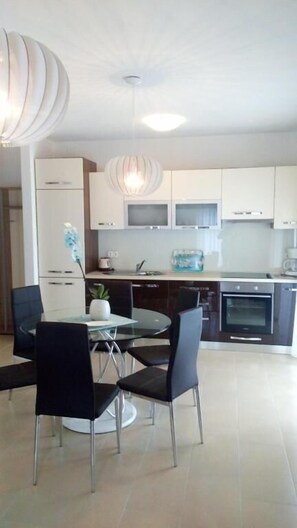 A modern kitchen with white cabinets, a dining table with chairs, and a pendant light. - Villa Duje Old town (Trogir)