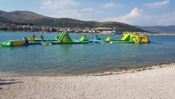 Ein Strand mit aufblasbaren Wasserspielgeräten und freiem Blick auf eine ferne Stadt.