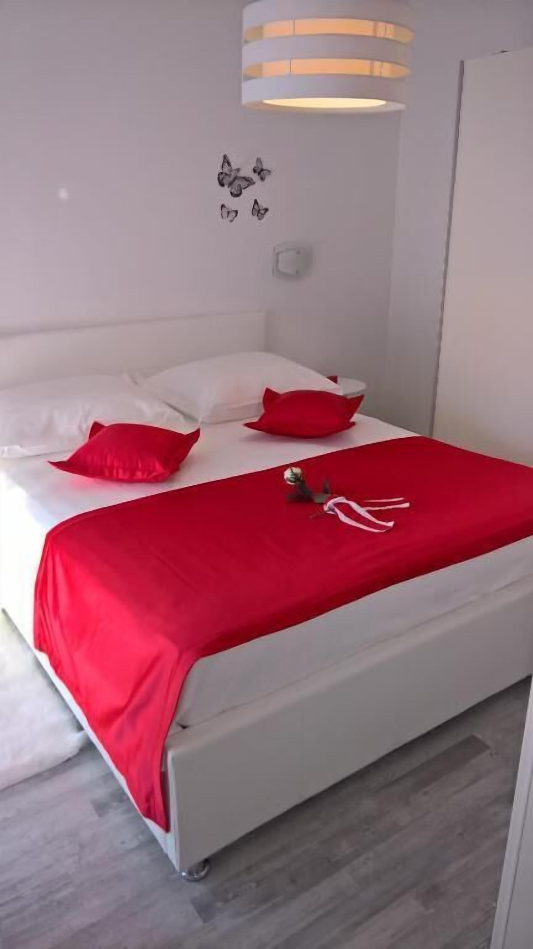 A bed with white bedding and red pillows, a red blanket, and a small decorative item on the bed.