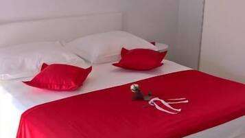 A bed with white bedding and red pillows, a red blanket, and a small decorative item on the bed.