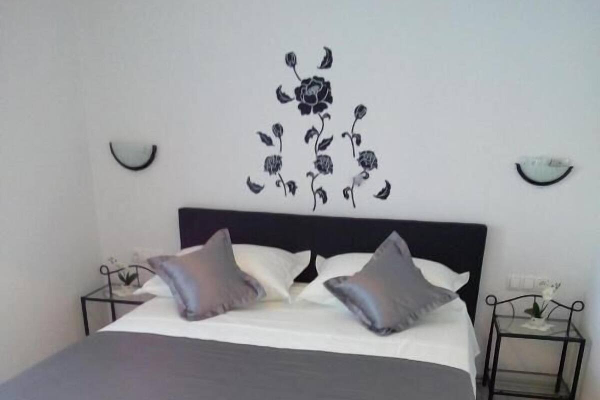 Un dormitorio con una cama grande, dos mesitas de noche y una lámpara fijada a la pared.