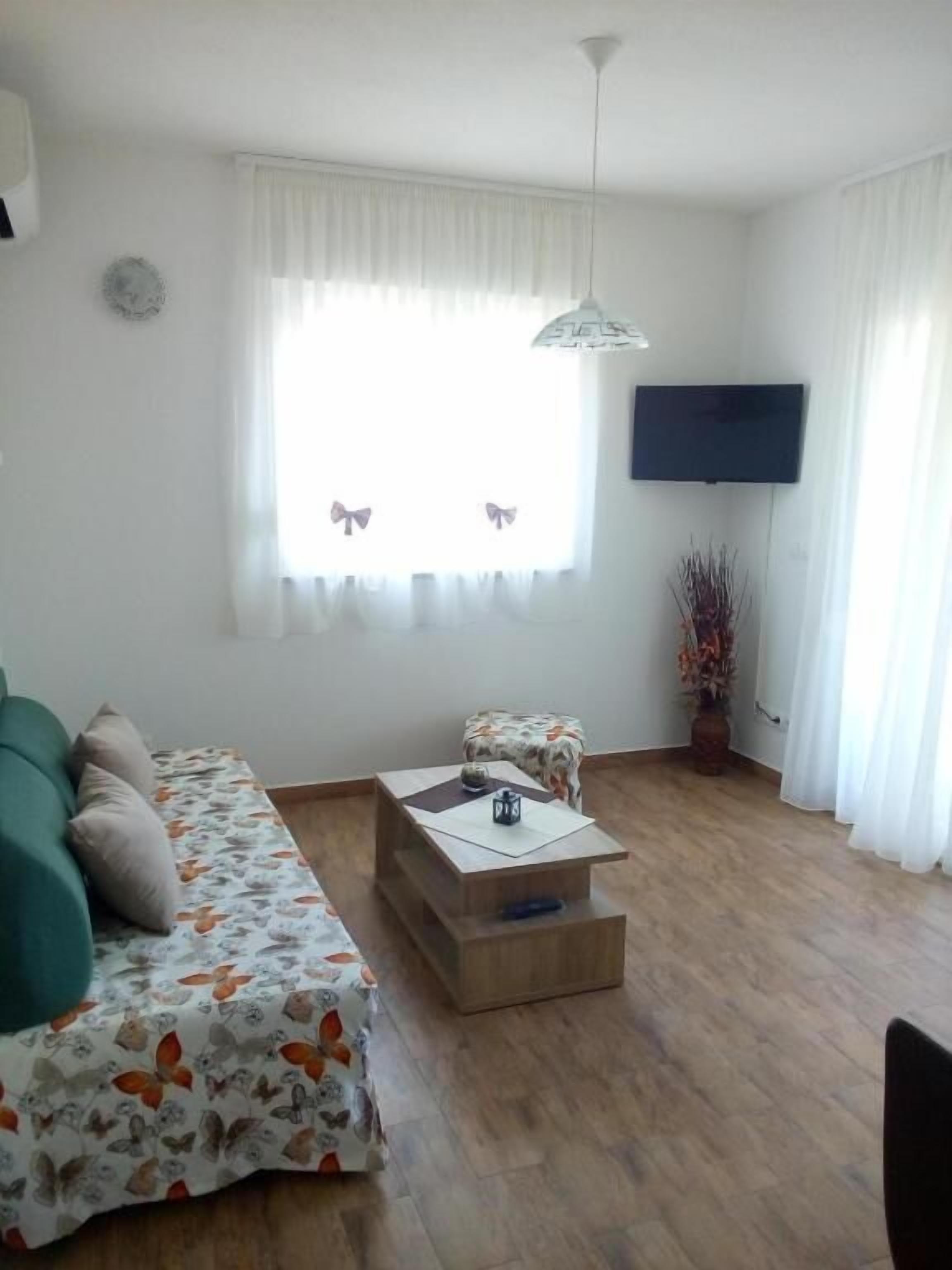 Una sala de estar con sofá, mesa de centro, televisor y ventana con cortinas.