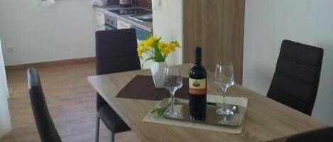 Un comedor con una mesa de madera, sillas negras, una botella de vino y un florero con flores.