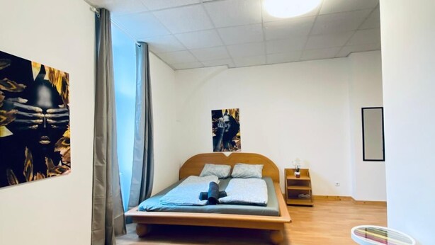 Un dormitorio con una cama de madera, una mesita de noche pequeña y un estante en la pared.