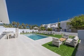 A modern outdoor pool area with a dining set, lounge chairs, and a well-maintained lawn. - Brand New 4 Bedroom Villa with private pool, 100 meters from the beach (Protaras)