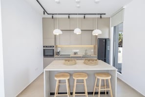 A modern kitchen with a central island, pendant lights, and wooden stools.