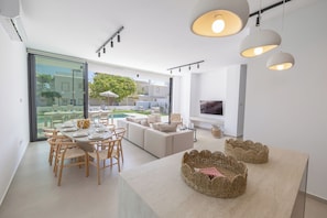 A modern living room with a dining area, large windows, and a flat-screen TV.