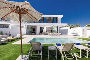 Une maison moderne dotée d’une piscine, d’un espace salon extérieur et d’un grand parasol.