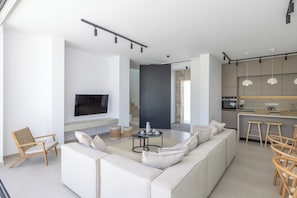 A modern living room with a sofa, a TV, a coffee table, and a kitchen area with stools.