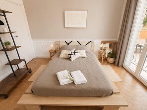 Une chambre à coucher bien rangée, avec un lit, des tables de chevet, une étagère fixée au mur et une fenêtre avec des rideaux.