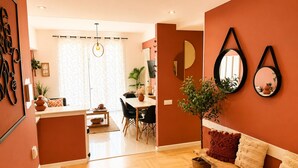 Ein modernes Wohnzimmer mit Holzboden, einer Couch, einem Essbereich mit Tisch und Stühlen sowie einer Küchenzeile mit Arbeitsplatte und Schränken.