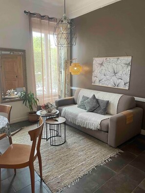 Un salon comprenant un canapé, une table basse, un fauteuil, un luminaire suspendu et une fenêtre avec des rideaux.