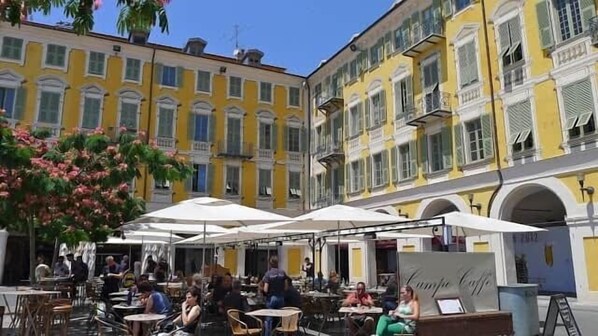 Un café en plein air, avec des tables et des chaises, entouré de bâtiments jaunes dotés de balcons.