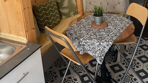 Ein gemütliches Zimmer mit Holzwand, einer Uhr, einem Schild, einem kleinen Tisch mit Pflanze und einem gemusterten Boden.