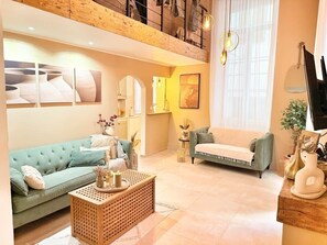 Amplia sala de estar con techo alto, un sofá verde, un sofá blanco y una mesa de centro de madera.