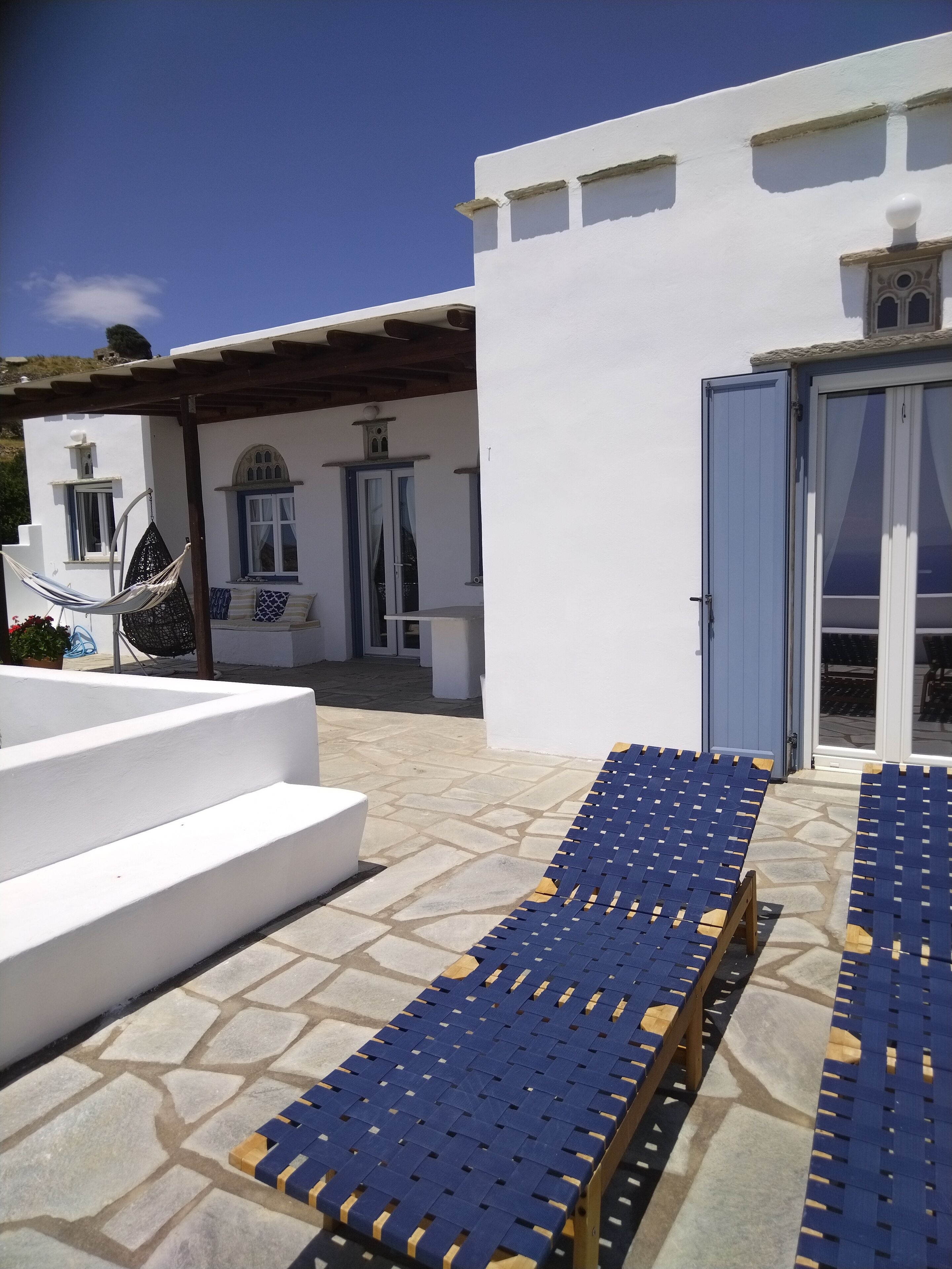 A white building with a stone patio, a hammock, and blue lounge chairs.