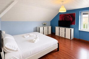 Une chambre à coucher avec un lit, une télévision, une commode et un tableau accroché au mur.