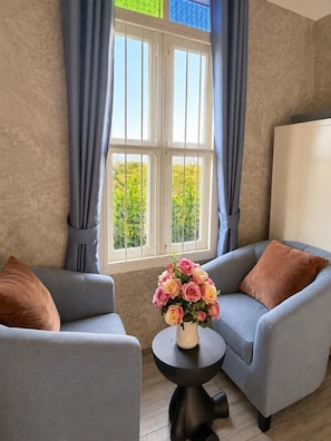 A room with two grey armchairs, a small black table with a vase of flowers, and a window with curtains. - Banana Village Resort (Mae Taeng)