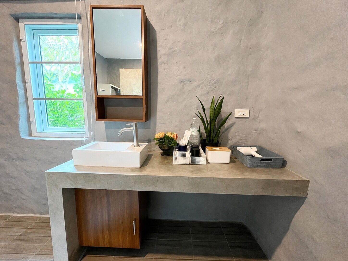 A bathroom with a white sink, a mirror, a potted plant, and a window with a view of greenery.