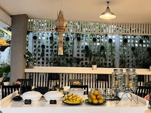 A buffet setup with food items, a decorative hanging lantern, and a wall with a grid of circular windows and plants.