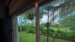 A window with a view of a well-maintained garden, a metal fence, and a door. - Banana Village Resort (Mae Taeng)