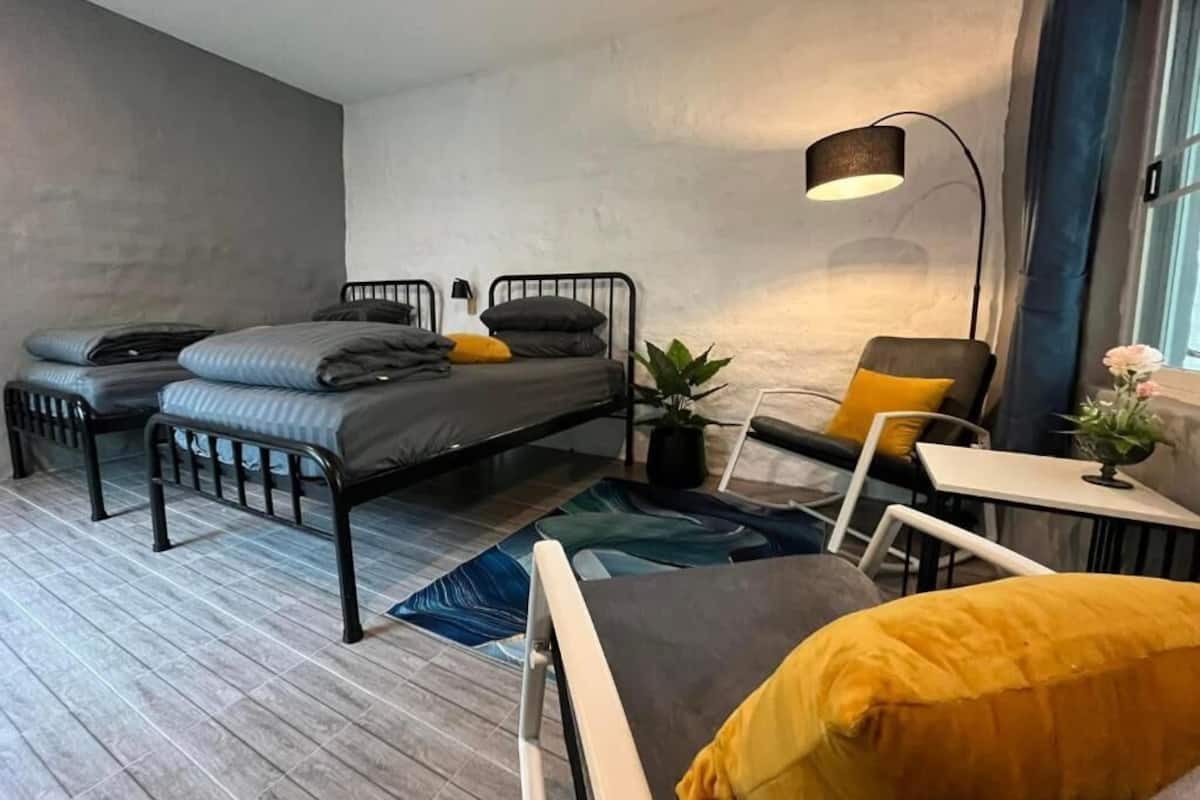 A modern bedroom with a bed, two chairs, a table, a lamp, and a potted plant.