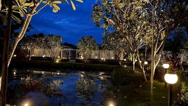 A nighttime outdoor area with a pond, trees, and illuminated structures. - Banana Village Resort (Mae Taeng)