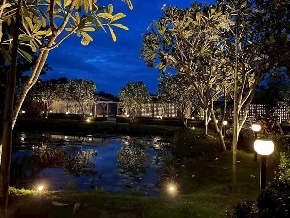 A nighttime outdoor area with a pond, trees, and illuminated structures.