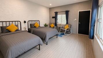 A bedroom with two beds, a chair, a small table, and a window with curtains.