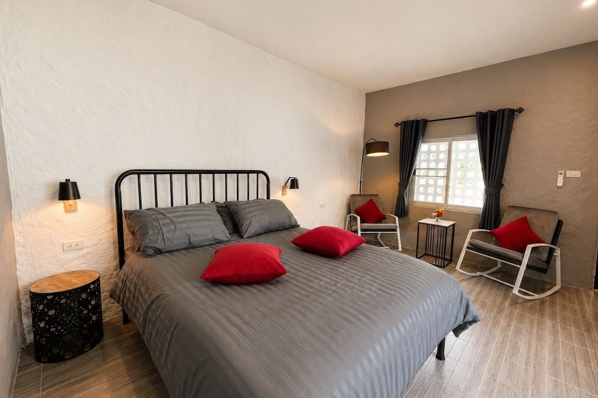 A bedroom with a bed, two bedside lamps, a chair, a small table, and a window with curtains.