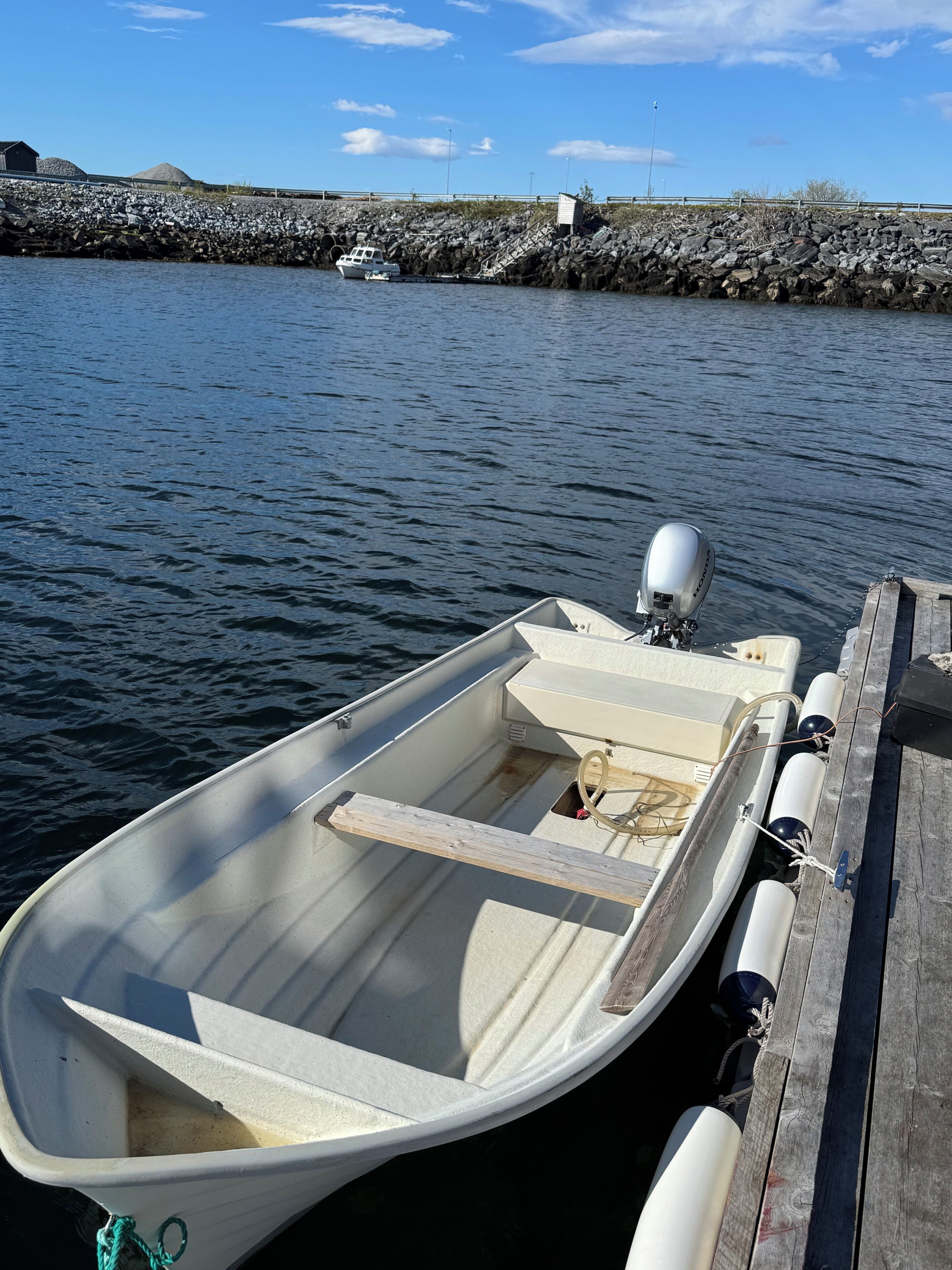 A small boat docked at a pier with a rocky shoreline in the background.