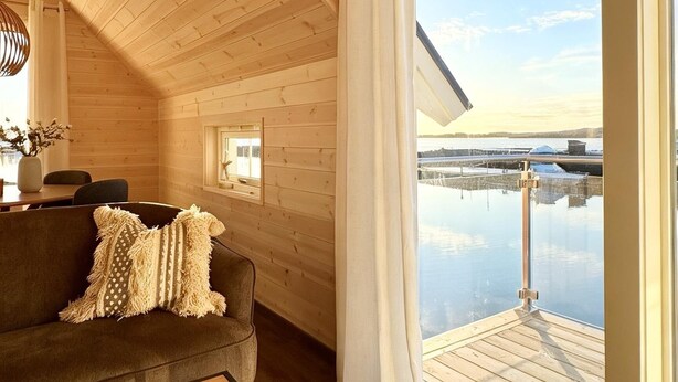 Un intérieur en bois donnant sur une étendue d’eau paisible, visible à travers une grande fenêtre.
