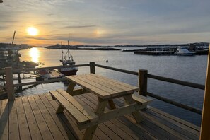 A wooden dock with a picnic table, a small boat, and a calm water body with boats in the background. - New and exclusive cabins with fantastic sea views, right by the sea. (Nordland)