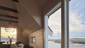Un intérieur moderne avec un plafond en bois, une grande fenêtre donnant sur un plan d’eau, un canapé gris et une table en bois.
