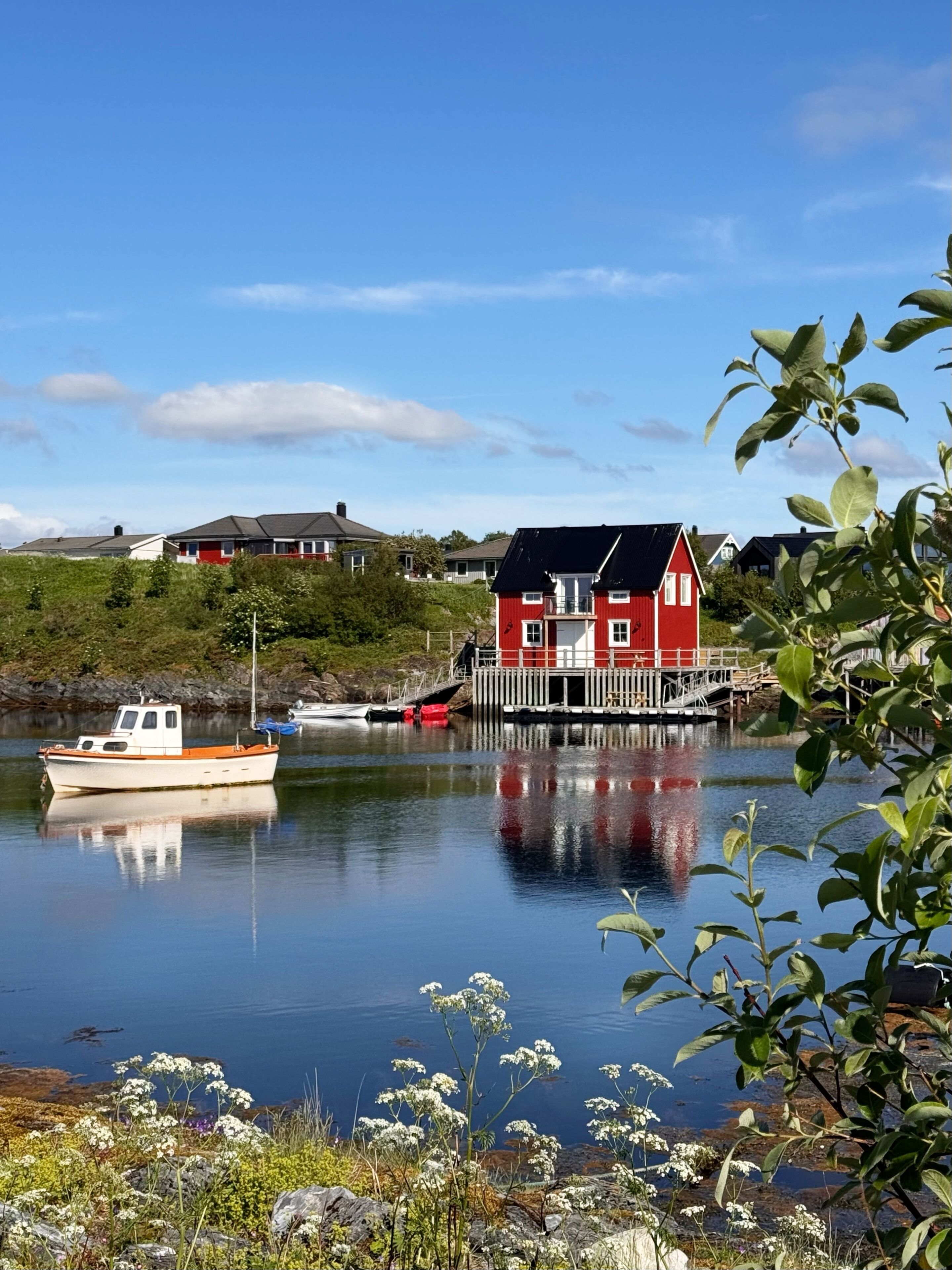 Un lago tranquilo con una casa roja, barcos y vegetación.