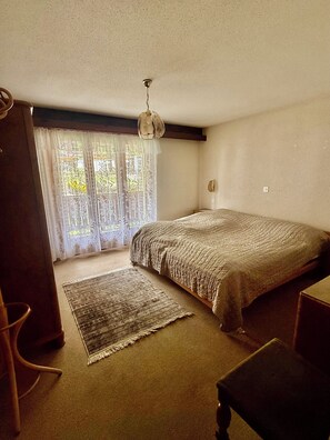 A bedroom with a bed, a rug, a chair, and a window with curtains. - Lovely vacation apartment with sun & mountain view (Saas-Fee)