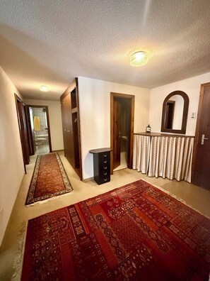 A hallway with a patterned carpet, a small black cabinet, a mirror, and a door leading to another room. - Lovely vacation apartment with sun & mountain view (Saas-Fee)