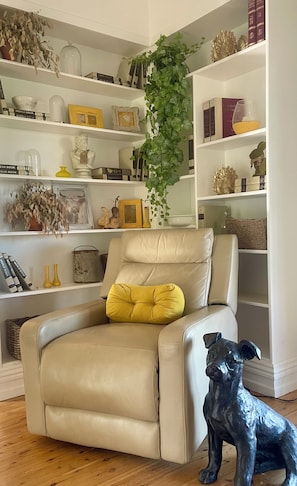A living room with a leather armchair, a dog statue, and shelves with books and decorative items.