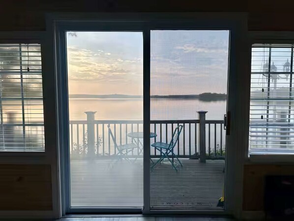 A view through a sliding glass door to a deck with a railing, a table, and chairs.