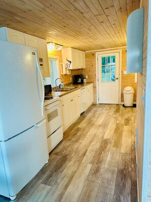 A kitchen with wooden cabinets, a refrigerator, a sink, and a door with windows.