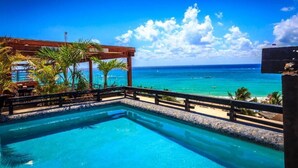 Una piscina con vista al océano, una pérgola de madera y palmeras.