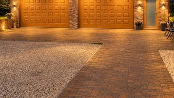 Une maison à deux étages avec une façade en briques, deux portes de garage et une allée gravillonnée.