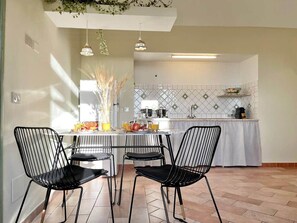 Eine moderne Küche mit Essbereich, mit weiß gefliestem Spritzschutz, schwarzen Metallstühlen und Pendelleuchten.