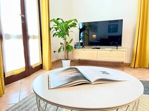 Una stanza con un tavolo rotondo, una pianta in vaso, una televisione a schermo piatto e un armadio.