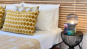 A bed with patterned pillows, a bedside table with a book, and a wall with abstract art.