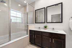 Un baño moderno con cabina de ducha de vidrio, dos lavamanos, armarios de madera oscura y una planta en maceta.