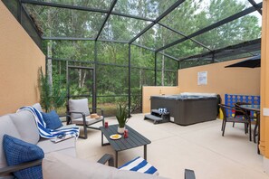 A covered outdoor patio with a sofa, chairs, a table, a hot tub, and a view of the forest. - Corvette Cove (Kissimmee)