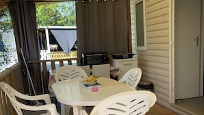 Une terrasse couverte avec une table et des chaises, un panier pour chien et un espace barbecue.
